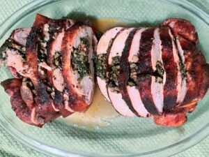 Sliced stuffed whole chicken with a browned, charred crust rests on a glass platter, showing a juicy pink interior and a hearty, inviting meal.
